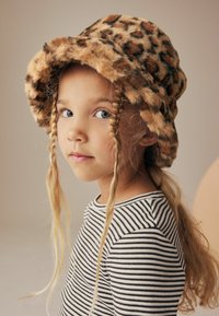 Leopardmønstret faux-fur bucket hat med bred skygge, parret med en stribet langærmet skjorte. Håret stylet i løse fletninger.