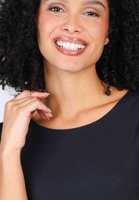 Black top with a wide neckline, smooth texture, and relaxed fit. Model displays a smiling expression with curly hair and natural nail polish.