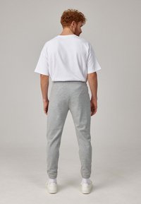 Gray sweatshirt pants with elastic cuffs, paired with a loose-fitting white cotton t-shirt. Background is a neutral light color.