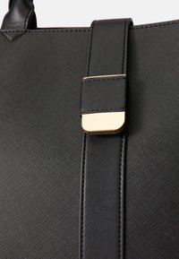 Geanta din piele texturată neagră, cu o curea netedă neagră și un accent din metal auriu, evidențiind un design minimalist și un finisaj elegant.