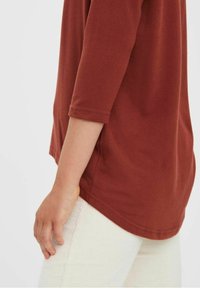 Haut couleur rouille à manches trois-quarts, en tissu doux. Pantalon en velours côtelé de couleur claire avec des rayures verticales et une surface texturée.