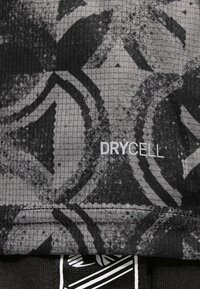 Tissu athlétique noir à surface texturée, avec un motif abstrait gris. L'étiquette "DRYCELL" est visible, indiquant des propriétés d'évacuation de l'humidité.