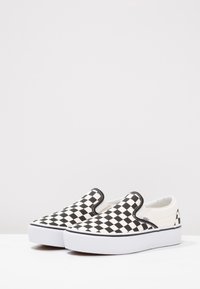 Crno-bijele karirane slip-on cipele s bijelim platformom i crnim šavovima, koje imaju gornji dio od platna i elastične strane.
