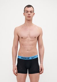 Sorte boxertruser med blå elastisk midje som har "NIKE"-merke. Stoffet har en glatt tekstur og subtilt mønster.