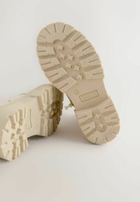 Beige rubber voetbalschoen zool met een textuurpatroon, voorzien van ribbels en stervormige accenten. Gemarkeerd met "BAKER" en maat "12."