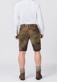 Shorts en cuir marron avec une texture usée, dotés d'une poche latérale et d'un détail de boucle à l'arrière, associés à une chemise blanche à manches longues.