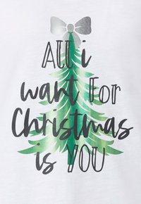 Biała koszula z zielonym motywem choinki, ozdobioną srebrną kokardą oraz napisem "All I want for Christmas is you" w kolorze czarnym i zielonym.