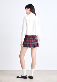 White button-up shirt, plaid mini skirt in red, blue, and green, black flats, and light gray ankle socks. Back view displays pleated design.
