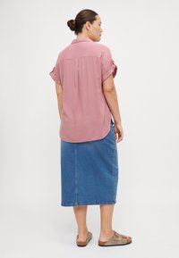 Blouse rose à manches courtes avec col, associée à une jupe midi en jean bleue. Les sandales possèdent deux sangles réglables. Texture de tissu lisse.