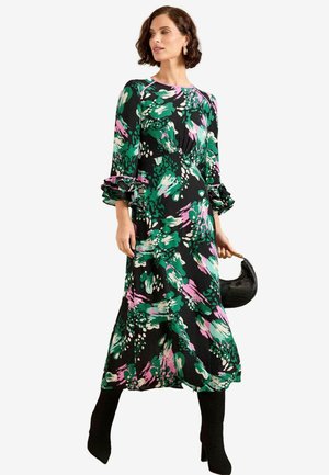 Abito nero a maniche lunghe con un vivace motivo floreale verde e rosa, con polsini arricciati, silhouette fluida, abbinato a una borsa nera.