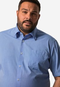 Lichtblauwe shirt met korte mouwen, een button-down kraag, een borstzak en een gestructureerde stof, met vijf bijpassende knopen aan de voorkant.