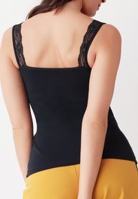 Zwarte tanktop met kantaccenten op de schouderbanden, getailleerde pasvorm en een soepele textuur. Draagt bij gele onderkleding, wat een casual stijl laat zien.