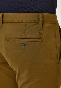 Brown cotton pants with a smooth texture, featuring a back pocket, button closure, and stitched waistband details.