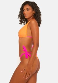 Top bikini arancione con design triangolare e spalline sottili, abbinato a slip a vita bassa con lacci laterali rosa. Texture liscia in tutta la mise.