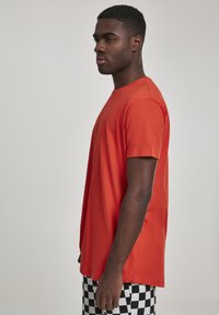 Rød t-skjorte med korte ermer og rund hals; laget av glatt stoff, med en løs passform og rett nederkant. Stylet med rutete shorts.