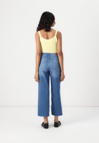 Yellow fitted tank top with thin straps, paired with high-waisted blue wide-leg jeans. Black flat shoes, smooth denim texture, minimal design.