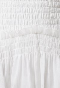 White dress featuring smocked texture with layered ruffles, lightweight fabric, subtle sheen, and a flowing design.