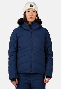 Giacca imbottita blu navy con design a zigzag, colletto alto e cappuccio in pelliccia removibile. Chiusura con zip e dettagli con tasche laterali.