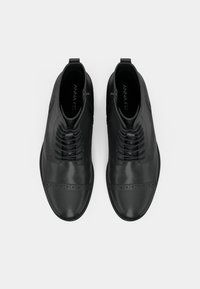 Melnas ādas potīšu zābaki ar gludu apdari, brogue detaļām uz pirksta un dekoratīvu šņorēšanu ar sānu rāvējslēdzēju.