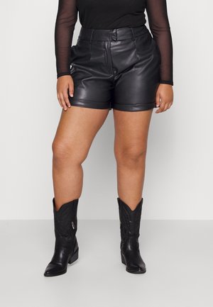 Mustat nahkahousut, joissa on sileä pinta, korkea vyötärö ja käänteet. Yhdistettynä polven ylle ulottuviin mustiin cowboy-kenkäisiin, joissa on koristeelliset ompeleet.