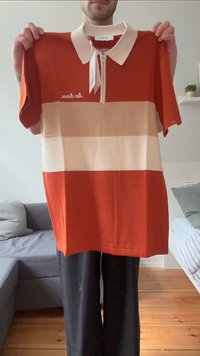 Polo shirt a maniche corte in arancione, crema e strisce beige. Presenta un colletto con zip e un logo sul petto. Il materiale sembra essere cotone.