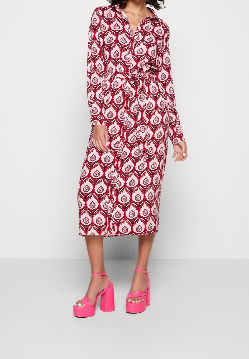Czerwona i biała midi sukienka w wzory z długimi rękawami i paskiem w talii, zestawiona z jasnoróżowymi sandałami na grubym obcasie.