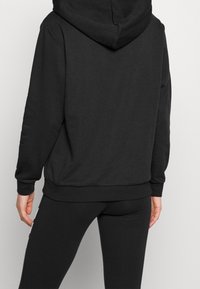Sweatshirt à capuche noir en tissu doux et texturé, à manches longues et coupe décontractée. Design simple sans logos ni motifs visibles.