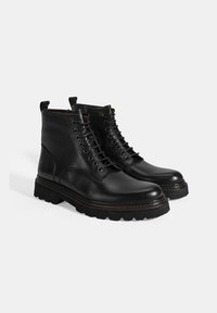 Zwarte leren enkelboots met een ronde neus, vetersluiting aan de voorkant en een contrasterende, textuur geprofileerde zool. Bevat een lus aan de achterkant voor het gemak bij het aantrekken.