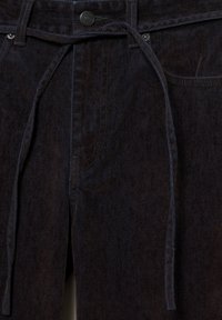 Tummat denimpantsit, joissa on teksturoitu pinta. Etutasku, napp closure ja solmuketju vyötäröllä säädettävää istuvuutta varten.