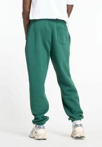 Gröna sweatpants med elastisk midja, med en bakficka och smalnande muddar. Matchas med grå och vita sneakers.