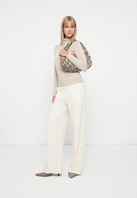 Pull en maille beige à col roulé, pantalon large blanc et sac à main en simili-cuir serpent marron. Des talons aiguilles beiges complètent la tenue.