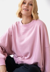 Przeciągający różowy sweter z miękkiego materiału, z okrągłym dekoltem i opadającymi szwami na ramionach, zapewniający luźny krój.