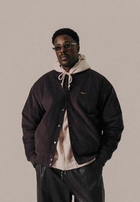 Dark purple corduroy jacket with snap buttons, layered over a light hoodie with a drawstring. Black pants complete the outfit.