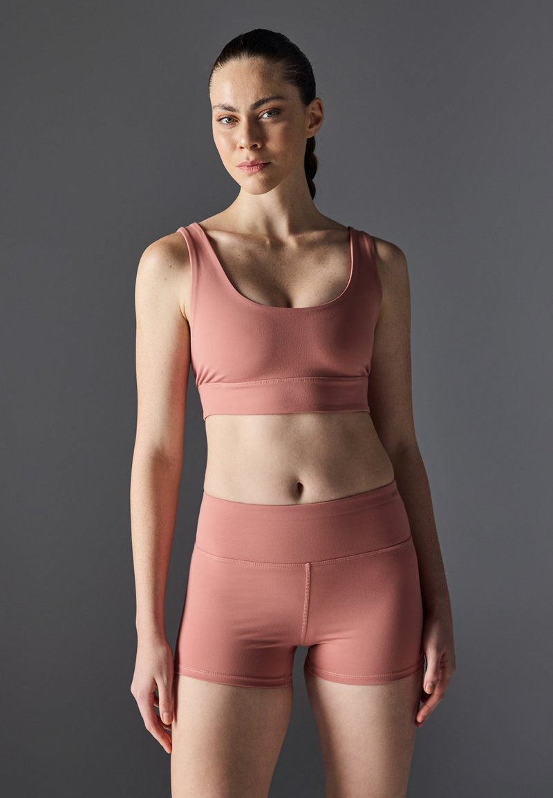 Lys rosa trenings-BH og shortser, laget av glatt, elastisk stoff. Har scoop-hals og høy midje-design.