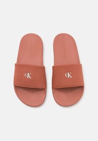 Sandales à glisser Calvin Klein, avec une sangle en tissu terracotta texturé et une semelle en caoutchouc, présentant un logo "CK" argenté sur la bande supérieure.