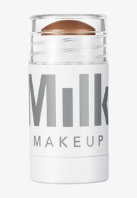 Milk Makeup Highlighter-Stick mit klarem, drehbarem Design. Weiße Hülle mit großen grauen Texten und einer gewölbten braunen Produktspitze.