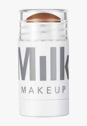 Milk Makeup Highlighter-Stick mit klarem, drehbarem Design. Weiße Hülle mit großen grauen Texten und einer gewölbten braunen Produktspitze.