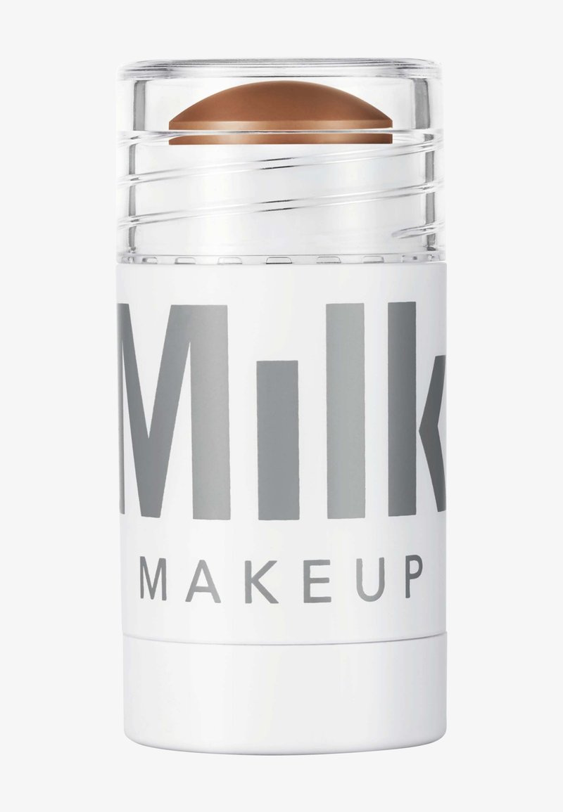 Milk Makeup Highlighter-Stick mit klarem, drehbarem Design. Weiße Hülle mit großen grauen Texten und einer gewölbten braunen Produktspitze.