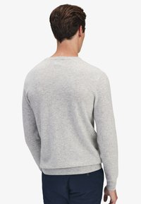 Ljusgrå tröja i mjukt material, med rund hals, långa ärmar och ribbade detalj vid handleder och nederkant. Bakifrån visas.