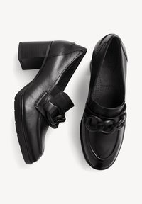 Chaussures en cuir noir à talon bloc avec un gros détail chaîne sur le devant, indiquées large largeur, vues de dessus et de côté sur fond blanc.