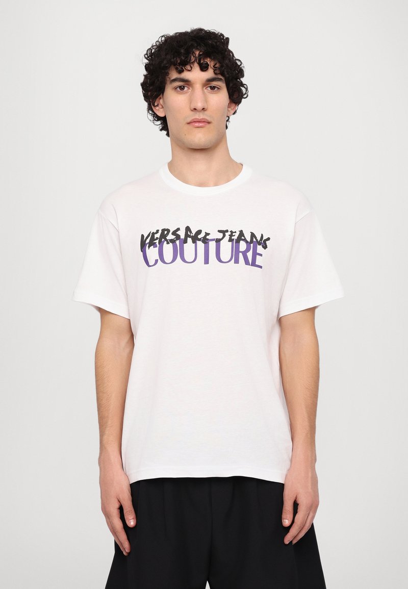 Biely bavlnený tričko s čiernym a fialovým textom "VERSACE JEANS COUTURE." Krátke rukávy, okrúhly výstrih, voľný strih.
