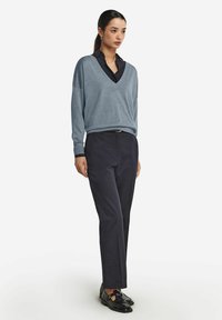 Jasnoniebieski sweter w serek z miękkiej dzianiny, w połączeniu z ciemnoniebieskimi spodniami. Czarne buty z detalem w postaci klamry. Prosty, luźny krój.