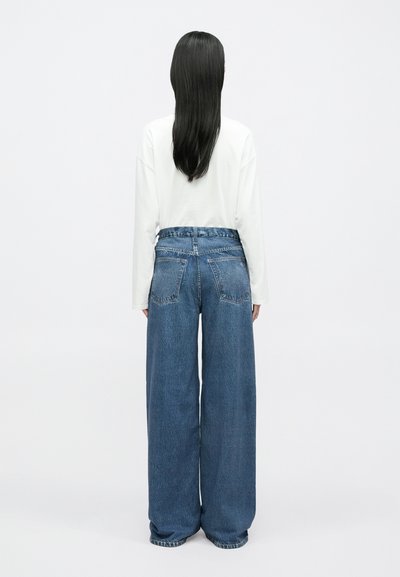 Szerokie niebieskie dżinsy z wysokim stanem, z wypłowiałym wykończeniem i podwójnymi tylnymi kieszeniami, w połączeniu z białą, długorękawową koszulą.
