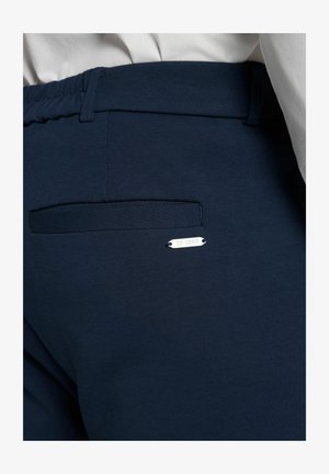 Marinefarbene Jogginghosen mit elastischem Bund, ausgestattet mit einer hinteren aufgesetzten Tasche und einem silbernen Metallanhänger mit der Aufschrift "JP 1880." Glatte Stoffstruktur.