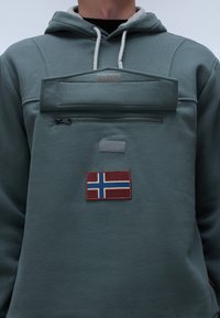 Groene fleece sweatshirt met een voorzak met rits, een verhoogde voorklap en een Noorse vlag patch. Voorzien van grijze koorden en accenten.