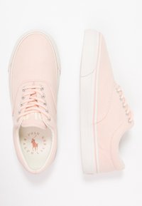 Světle růžové plátěné tenisky s bílými gumovými podrážkami, kulatou špičkou a stříbrnými očky na tkaničky. Uvnitř se nachází značka v kontrastních barvách.