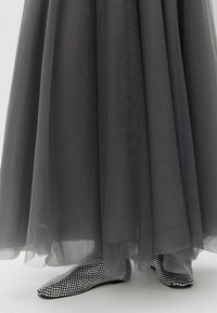 Hallhalline maksisärk, mis on kihiline mustade madalate kingade kohal, millel on hõbedased sädelevad rhinestone'id, tuues esile tekstuurse ja särava pinna.