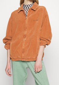 Kurtka na zamek z sztruksu w spalonym pomarańczowym kolorze, z kołnierzykiem, elastycznymi mankietami i marszczonym dołem. Posiada subtelne haftowane logo "BGC Jeans".
