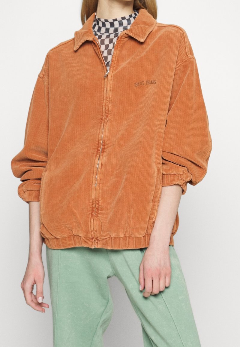 Kurtka na zamek z sztruksu w spalonym pomarańczowym kolorze, z kołnierzykiem, elastycznymi mankietami i marszczonym dołem. Posiada subtelne haftowane logo "BGC Jeans".