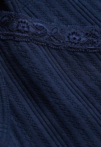 Tissu bleu foncé avec une texture côtelée verticale et une bordure en dentelle horizontale avec des motifs floraux.